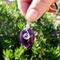 Deep purple Amethyst keychain with silver wire wrap, shown in close up outdoors in front of green bush for natural contrast.